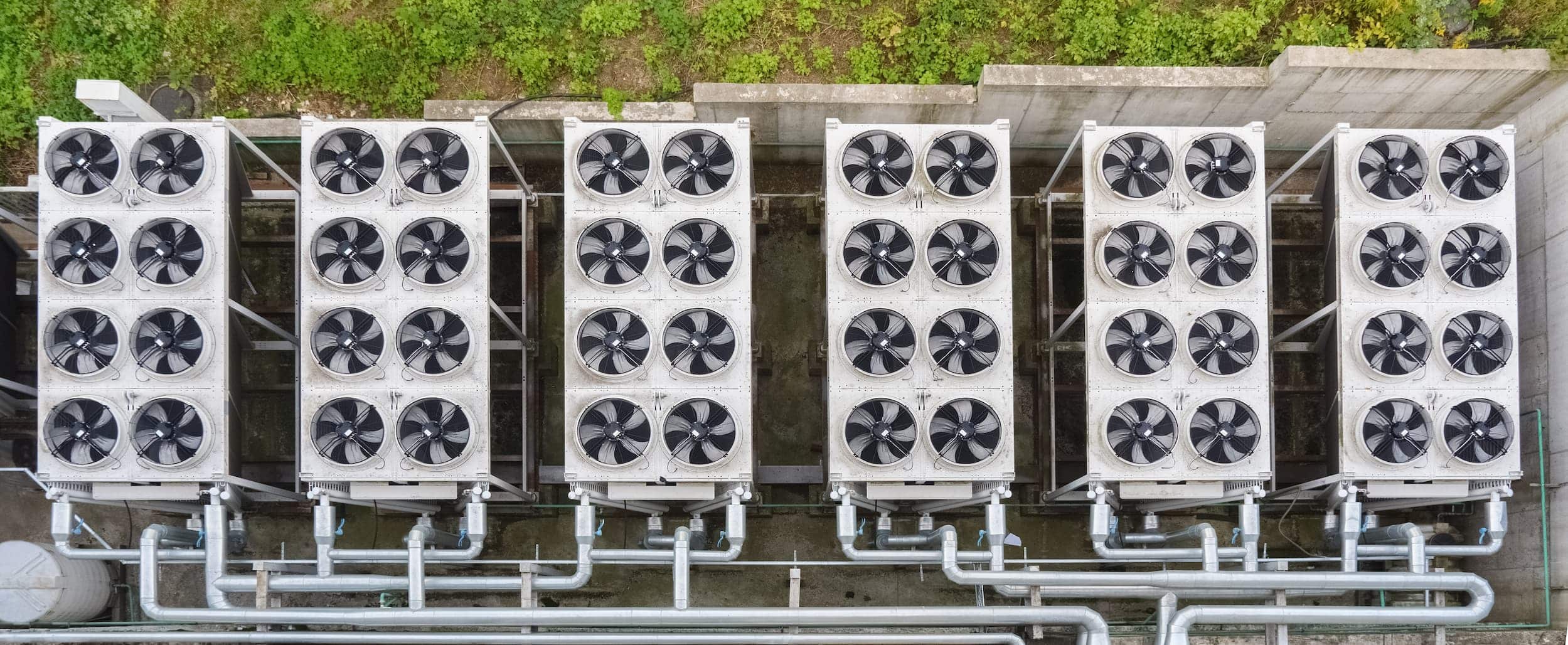 Aerial view of six industrial HVAC units arranged in two rows, with visible fans and pipes, set against a grassy background. - Southland Mechanical: Industrial Strength HVAC