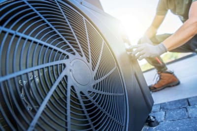 Close-up of a technician adjusting a large HVAC unit outdoors, with sunlight visible in the background. - Southland Mechanical: Industrial Strength HVAC